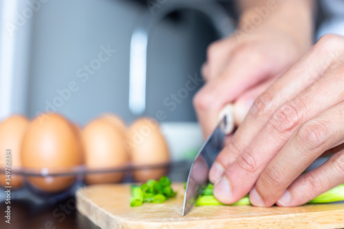 closeup of people hand and knife slice spring onion on wood butcher and fresh chicken egg in bowl and group of egg in box on wooden kitchen table for healthy and delicious meal or food dinner cook