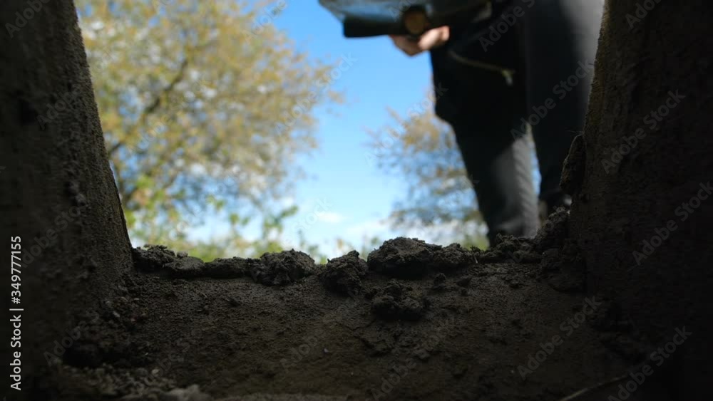 An unrecognizable person in dark clothes is digging a square pit against a blue sky with clouds. Point of view from the grave into which soil is sprinkled from shovel.  Slow motion 200 fps
