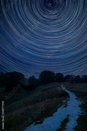 Digital composite image of star trails around Polaris with Stunning inspirational Summer landscape image over English countryside with mist hanging in fields