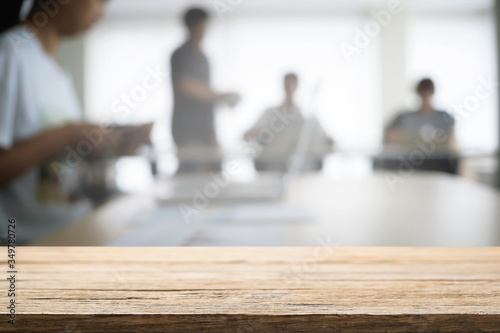 Empty wooden desk space over blurred office or meeting room background. Product display.