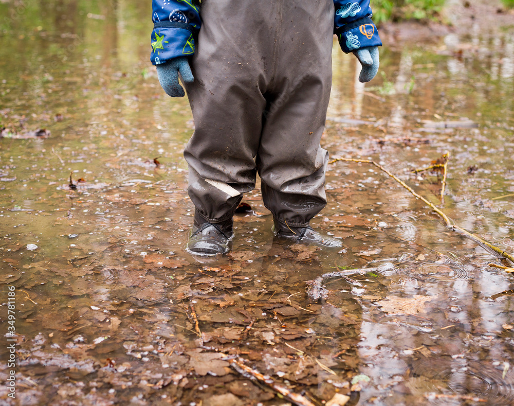 child in rubber boots stands in a puddle child in rubber boots stands in a puddle