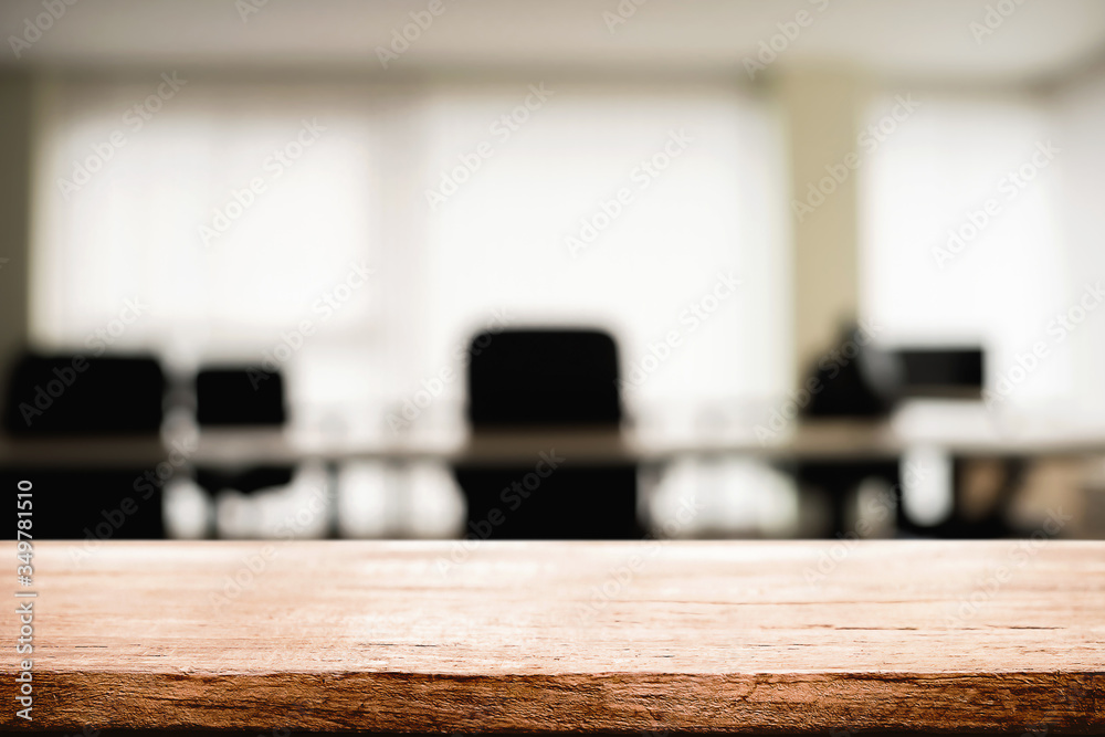Empty wooden desk space over blurred office or meeting room background. Product display.