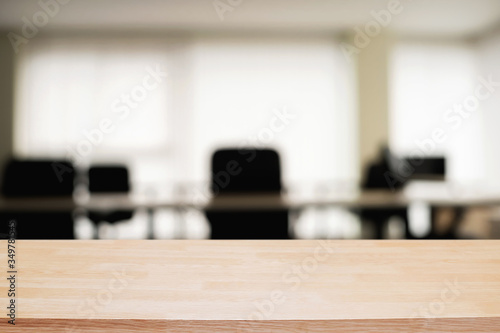 Empty wooden desk space over blurred office or meeting room background. Product display.