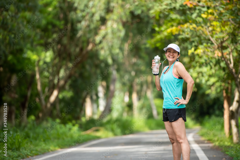 Healthy athletic asian woman is drinking pure water from the bottle refreshing herself after exercise in the nature park. Healthy and Lifestyle Concept