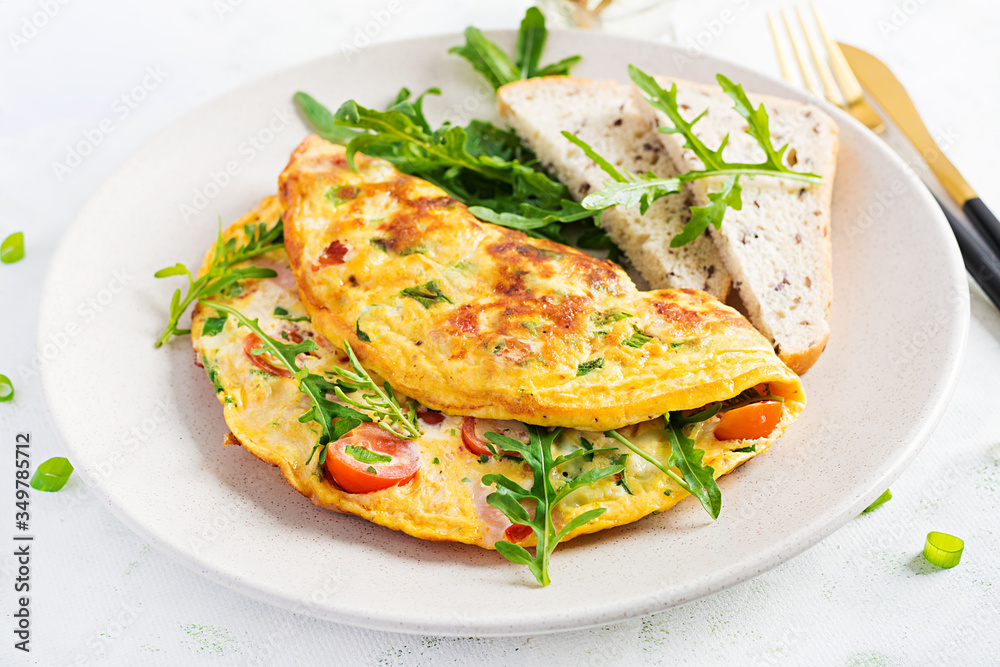 Omelette with tomatoes, ham, cheese and green herbs on plate. Frittata - italian omelet. Omelette with tomatoes, ham, cheese and green herbs on plate. Frittata - italian omelet.