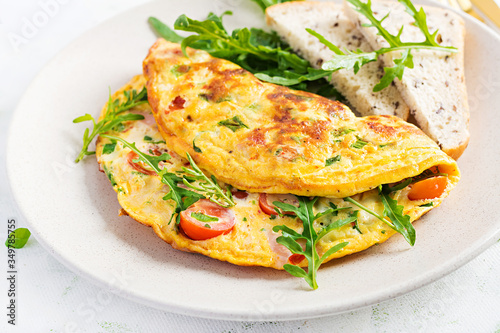 Omelette with tomatoes, ham, cheese and green herbs on plate. Frittata - italian omelet.