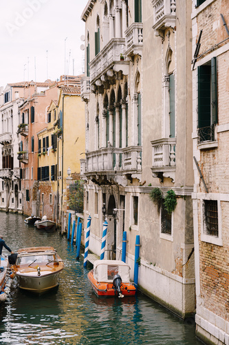 Boats moored at the walls of a building in a canal in Venice, Italy. Classic Venetian street views - wooden shutters, brick houses, bridges