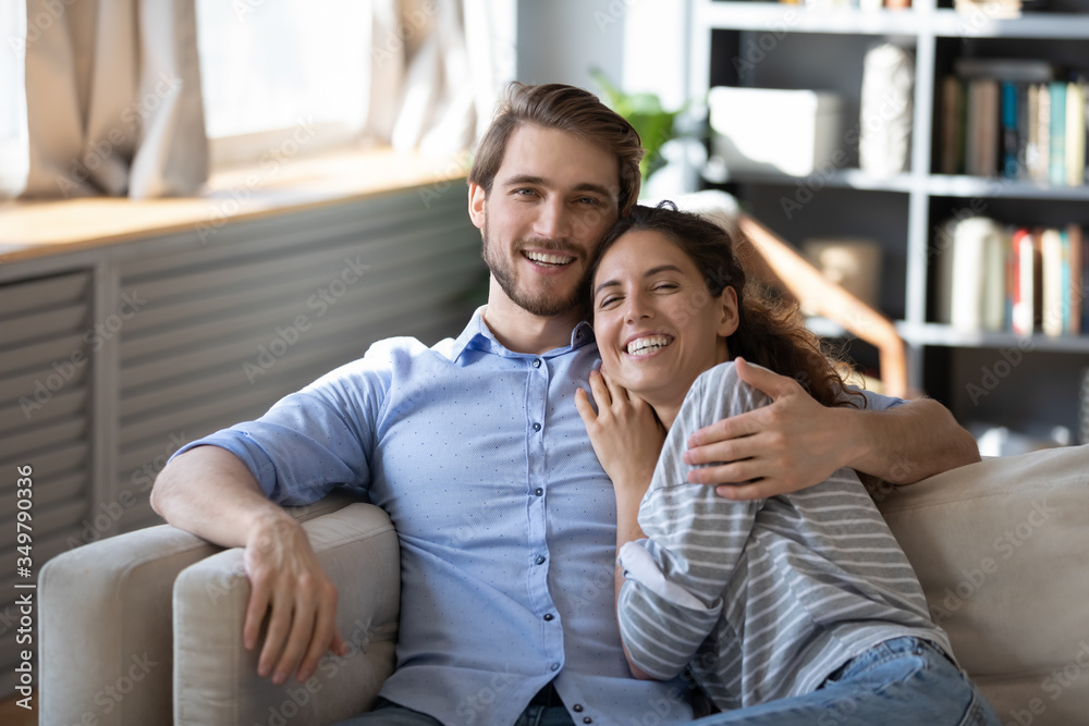 Portrait of happy Caucasian couple sit relax on couch in living room hugging cuddling, smiling millennial man and woman rest on sofa at home, embrace show love and affection, relationships concept Portrait of happy Caucasian couple sit relax on couch in living room hugging cuddling, smiling millennial man and woman rest on sofa at home, embrace show love and affection, relationships concept