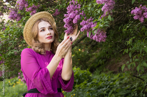 Young woman in straw hat enjoys the scent of blossoming lilac