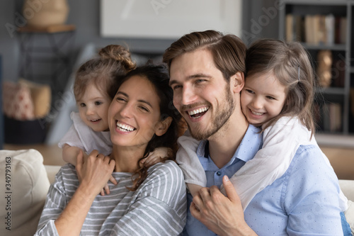 Overjoyed young Caucasian family with little daughters hug cuddle enjoy weekend at home together, smiling happy parents with small girls kids have fun playing, show love and unity, bonding concept