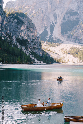 Wedding couple sailing in a wooden boat at the Lago di Braies in Italy. Newlyweds in Europe, on Braies lake, in the Dolomites. The groom rows the oars, the bride sits opposite him.