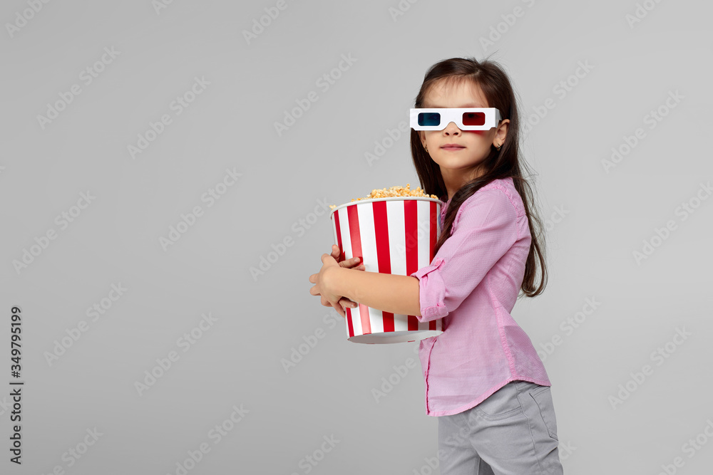 cute child girl wearing red-blue 3d glasses having fun and holding popcorn bucket isolated on gray background. copy space cute child girl wearing red-blue 3d glasses having fun and holding popcorn bucket isolated on gray background. copy space