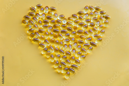 Heart shape of yellow vitamin supplements, omega 3 capsules, loving health dietary on bright background with copy space