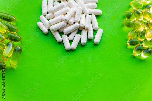 Groups of white vitamin supplements with stack of yellow jelly pills, health dietary capsules on bright green background with copy space
