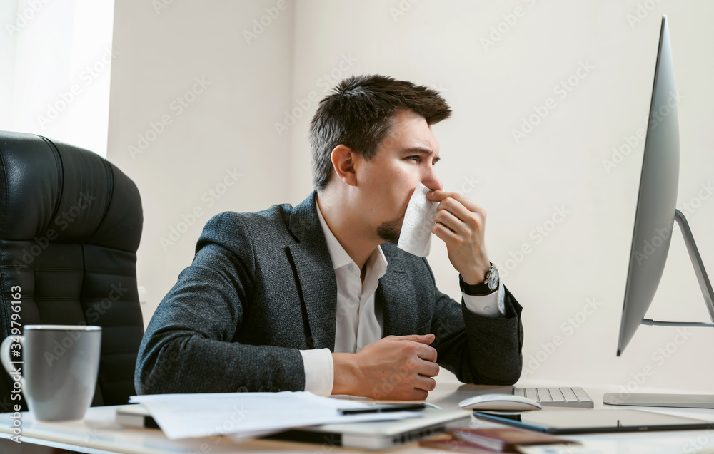 A young businessman or office worker sneezes, coughs, blows his nose at the workplace. Overworked worker got colds and flu. High temperature with ARVI or SARS. Epidemic of influenza or coronavirus. A young businessman or office worker sneezes, coughs, blows his nose at the workplace. Overworked worker got colds and flu. High temperature with ARVI or SARS. Epidemic of influenza or coronavirus.
