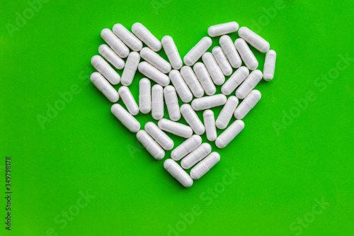 Heart shape of white vitamin supplements, loving health dietary capsule pills on bright green background with copy space