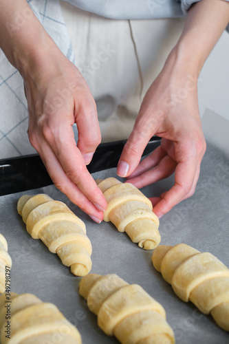 A woman is cooking croissants. Prepare for baking. Delicious traditional french crispy croissants for breakfast. Homemade bakery, cuisine for family. Girl chef work on kitchen table. Raw croissants