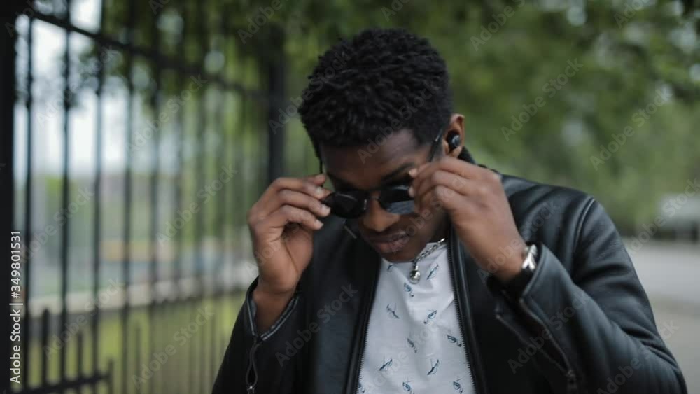 Stylish African American man wearing sunglasses walking in a summer city puts on fashionable eyewear Stylish African American man wearing sunglasses walking in a summer city puts on fashionable eyewear