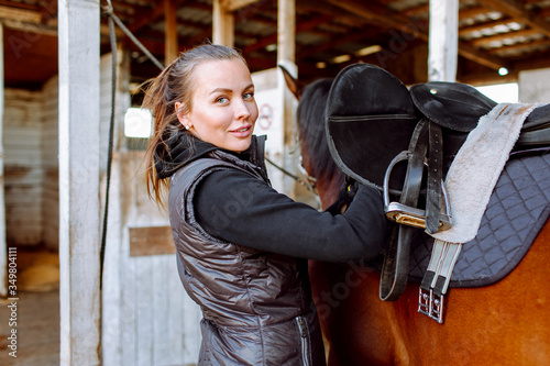 Portrait beautiful smiling woman long hair next to her horse in a stable. Horseback riding
