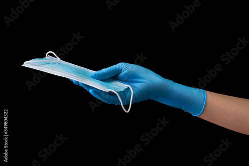 Doctor's hand in medical gloves holding a mask isolated on black