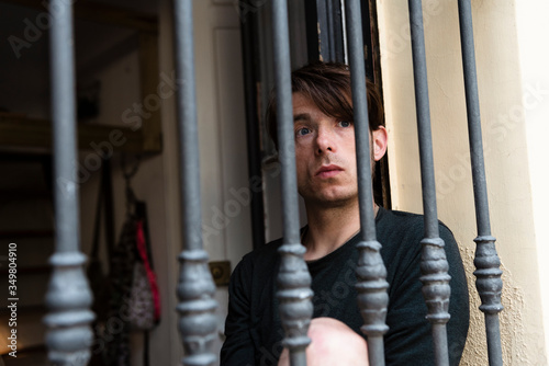 Young man looking through a barred window