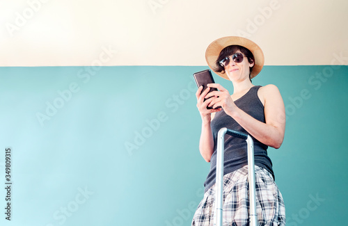 Woman in skirt, with straw hat and striped shirt prepared with a red suitcase and her face mask for her vacation in Covid's time.