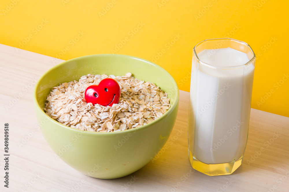 oatmeal in a green bowl with a red happy heart and a glass of milk on a wooden table, health care, dietary and proper food, gluten and lactose tolerance, yellow background oatmeal in a green bowl with a red happy heart and a glass of milk on a wooden table, health care, dietary and proper food, gluten and lactose tolerance, yellow background