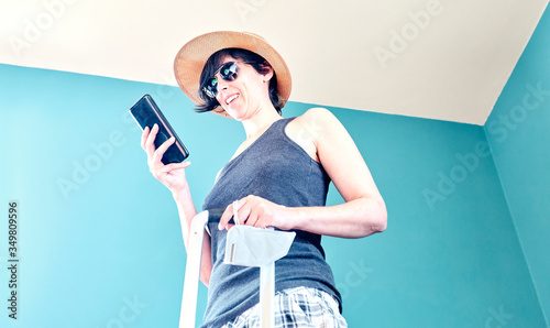 Woman in skirt, with straw hat and striped shirt prepared with a red suitcase and her face mask for her vacation in Covid's time.