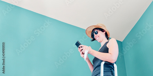 Woman in skirt, with straw hat and striped shirt prepared with a red suitcase and her face mask for her vacation in Covid's time.