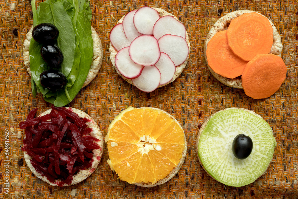vegetarian sandwiches. on grain loaves lie. repeating the shape of the circle radishes, green radishes, carrots, beets cut into strips, olives, sorrel and orange. it harmonizes with a warm textured da