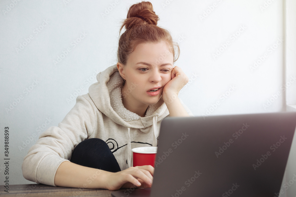 Young Caucasian woman looking bored in front of laptop at home. Work from home concept Young Caucasian woman looking bored in front of laptop at home. Work from home concept