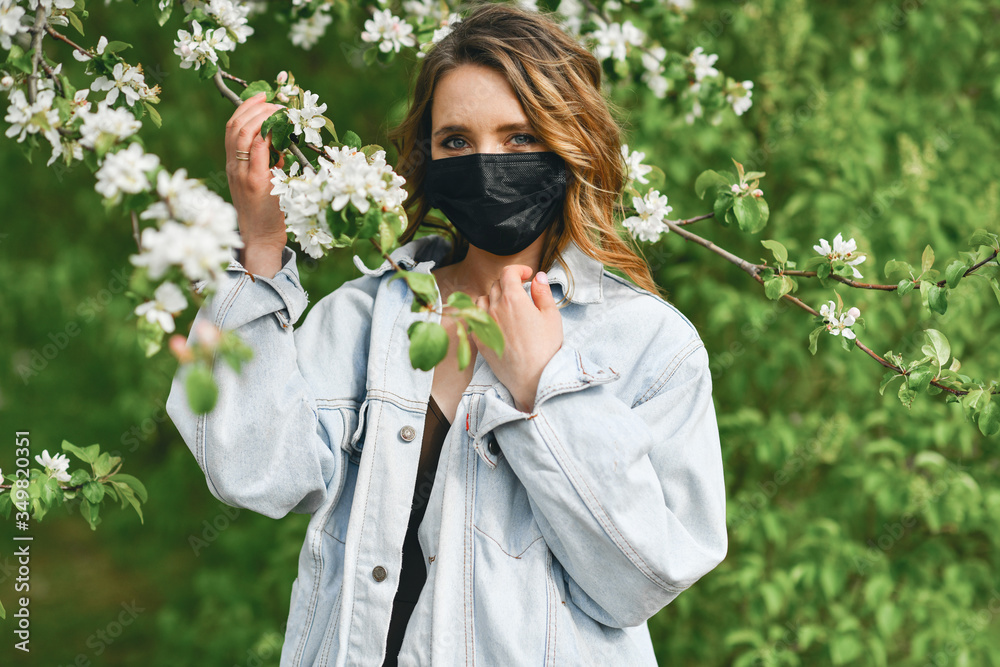 Girl in medical mask on background blooming apple tree. Concept and symbol end quarantine COVID-19 and pandemic coronavirus. Protection against virus and allergy in flowering garden in spring 2020 Girl in medical mask on background blooming apple tree. Concept and symbol end quarantine COVID-19 and pandemic coronavirus. Protection against virus and allergy in flowering garden in spring 2020