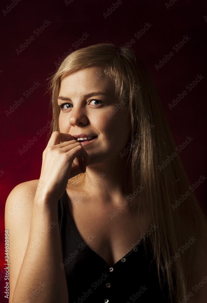 Young beautiful blonde on a dark red background. Close-up of the red lips of a seductive girl raising a finger to her mouth. Flirtation. Young beautiful blonde on a dark red background. Close-up of the red lips of a seductive girl raising a finger to her mouth. Flirtation.