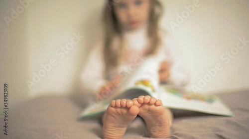 little girl reading a book sitting, baby feet close-up, bare feet