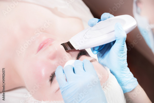 Close-up ultrasound face peel at the beautician. Beautician squeezes acne on the patient's forehead with a medical needle. Face next to hands in blue gloves of cosmologist