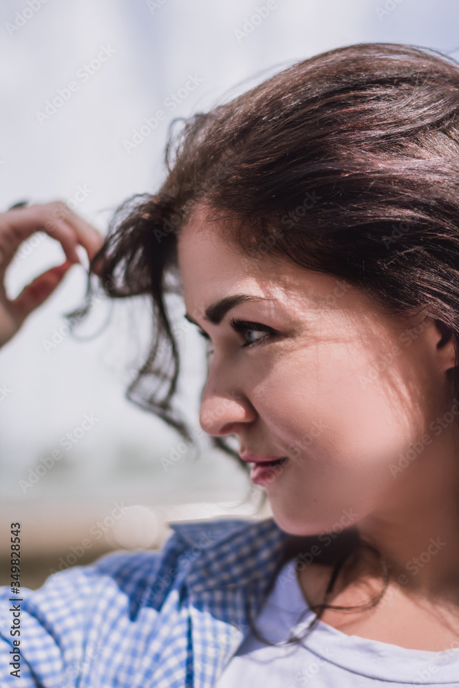 Portrait of a beautiful brunet girl touching her thick wavy hair. Young girl in a blue shirt and pink wrist watch by the fountain enjoying the sun. Concept of beauty, youth, student and joy Portrait of a beautiful brunet girl touching her thick wavy hair. Young girl in a blue shirt and pink wrist watch by the fountain enjoying the sun. Concept of beauty, youth, student and joy