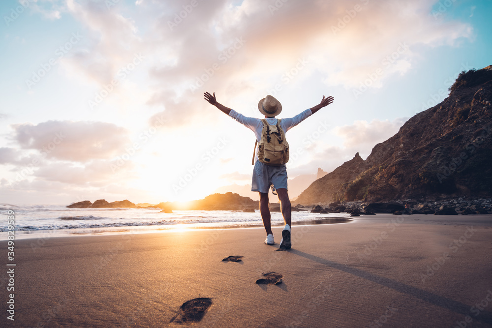 Plakat Young man arms outstretched by the sea at sunrise enjoying freedom and life, people travel wellbeing concept