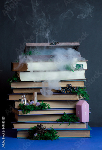 Mystery wooden box on stacks of the books with some tiny things. moss, steam on dark background. Magical atmosphere