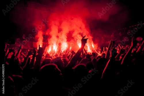 Red fire in the crowd. Big crowd at the festival. Fans burn prohibited fireworks. Dangerous red fireworks in the crowd.