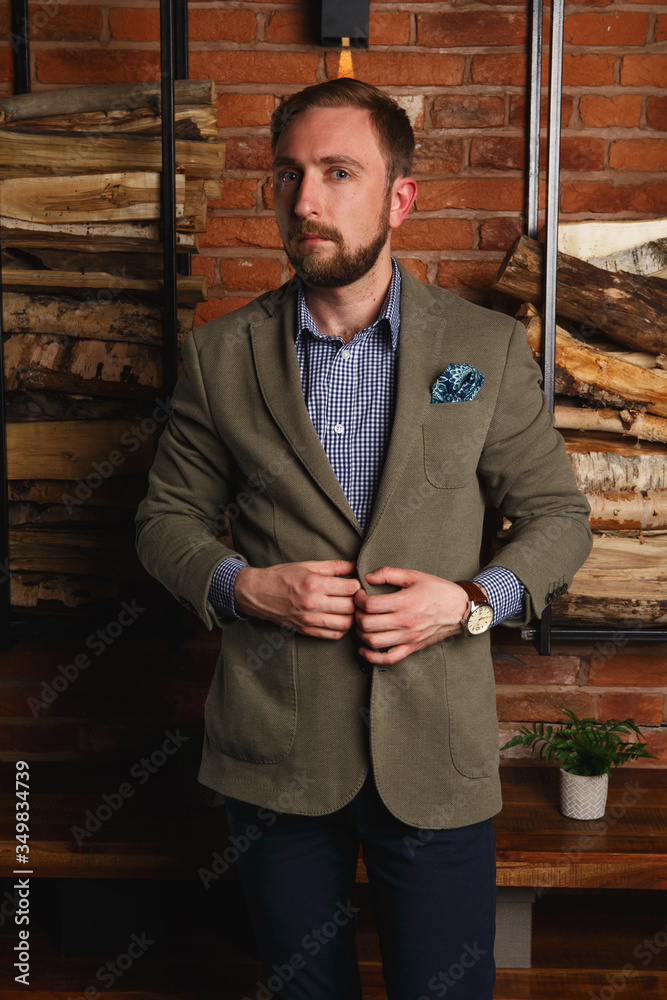 Side view of young fashion man in stylith blaizer standing in modern loft interior