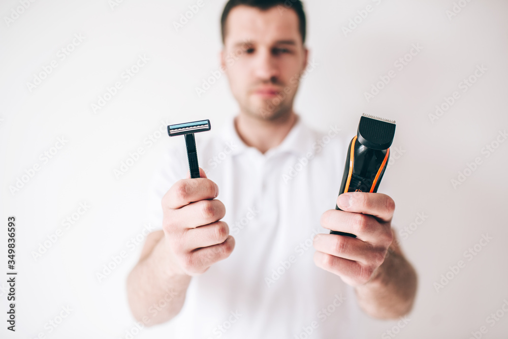 Young man isolated over white background. Serious guy hold shaving machine and razor in hands. Difficult choice. Manual or electric shaving. Young man isolated over white background. Serious guy hold shaving machine and razor in hands. Difficult choice. Manual or electric shaving.