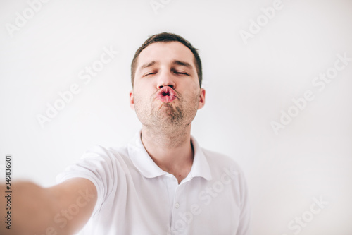 Young man isolated over white background. Ridiculous guy hold lips together like duck. Kissing mode. Funny posing on camera. Hold it with hand.