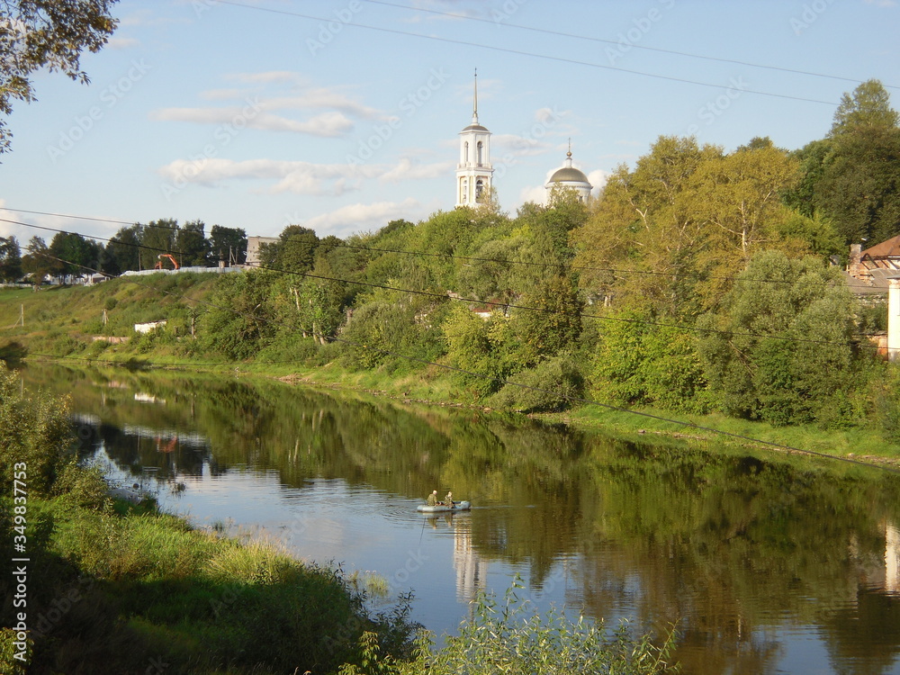 Fishermen on the river green trees and a temple in Torzhok, Russia
