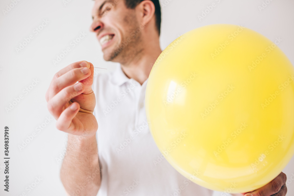 Young man isolated over white background. Guy pierce a balloon with needle. Afraid of sound. Cut view and close up. Defocused guy on picture. Young man isolated over white background. Guy pierce a balloon with needle. Afraid of sound. Cut view and close up. Defocused guy on picture.