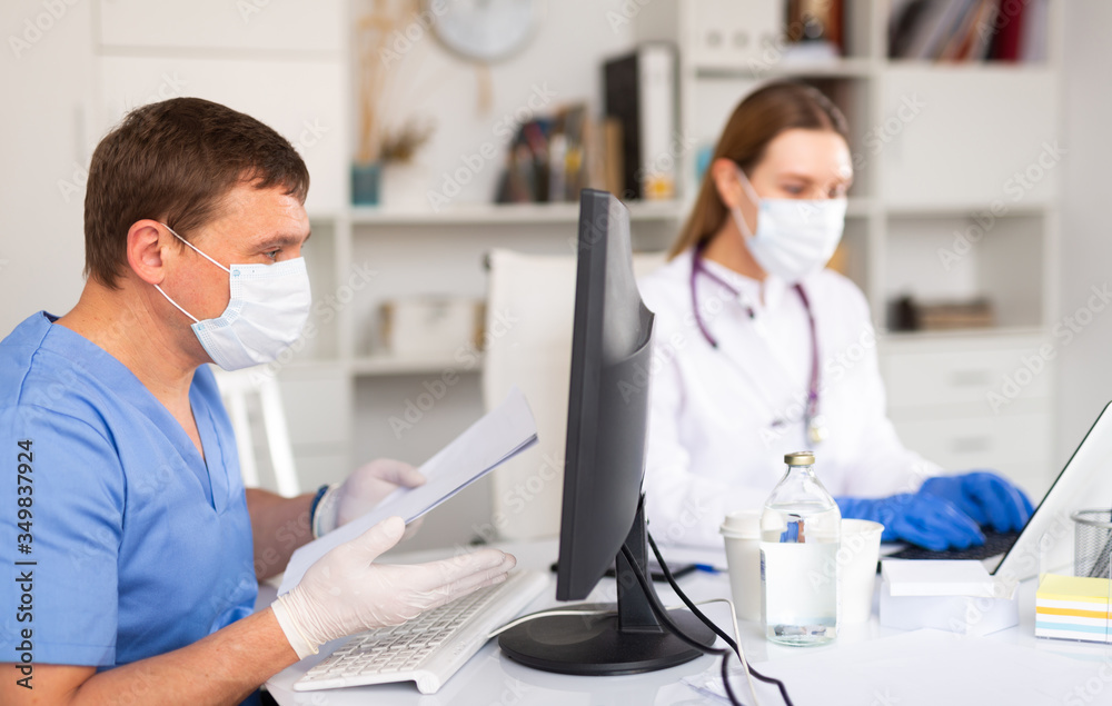 Doctor and nurse in protective mask check patient data in hospital computer database