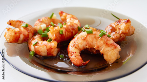 Large fried pacific prawns in spicy chili sauce with chopped green onions on a glass plate.