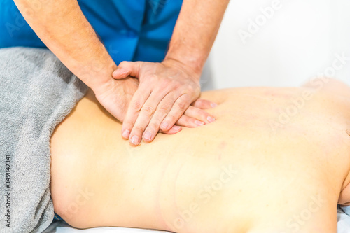 Massage with two hands on the kidneys to a young patient lying on her stomach. Physiotherapy safety measures in the Covid-19 pandemic. Osteopathy, therapeutic chiromassage