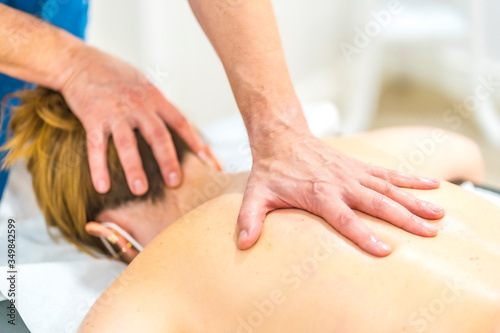 Physiotherapist performing a massage with one hand on the back of a girl with a mask. Physiotherapy safety measures in the Covid-19 pandemic. Osteopathy, therapeutic chiromassage