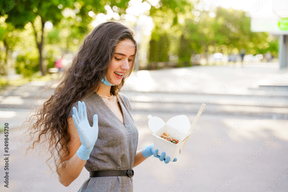 Young surprised girl with curly hair in medical gloves and mask holds wok  in box in