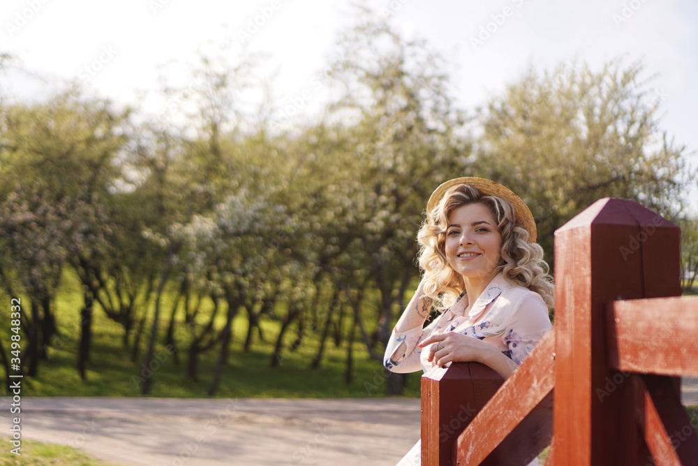 Beautiful woman in a white summer dress and a straw hat stands on a birch bridge in the park Beautiful woman in a white summer dress and a straw hat stands on a birch bridge in the park